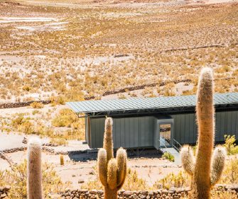Desert terrain with tall cacti overlooking a small lodge and distant plains.