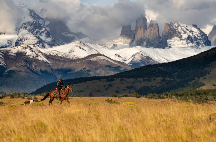 A gaucho on a horse, with his dog and the towers in the background in Torres del Paine, conservation reserve