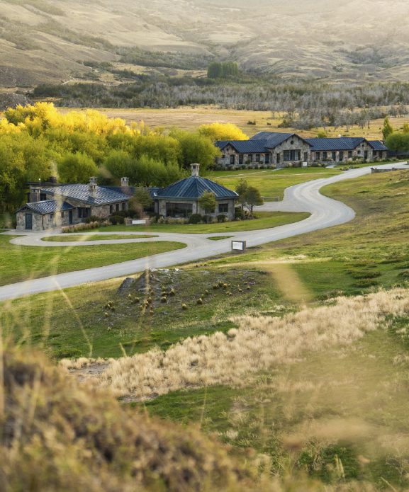 Contemporary Explora lodge buildings framed by trees and dramatic snow‑capped mountains in Patagonia National Park.
