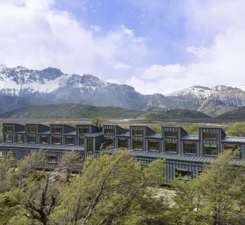 Explora El Chaltén lodge in Argentine Patagonia, overlooking a glacier‑fed lake with the dramatic granite peaks of Los Glaciares National Park in the background.
