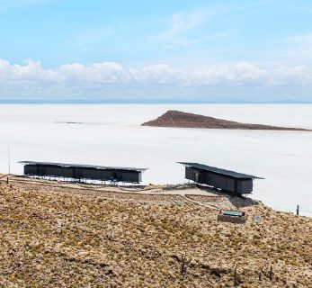Minimalist Explora lodge structures overlooking vast white salt flats, with volcanic terrain under a clear desert sky in Atacama.