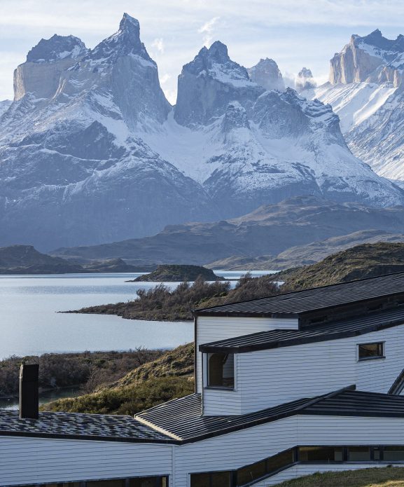 Explora Torres del Paine lodge overlooking a lake, with the iconic granite peaks of Torres del Paine rising in the background.
