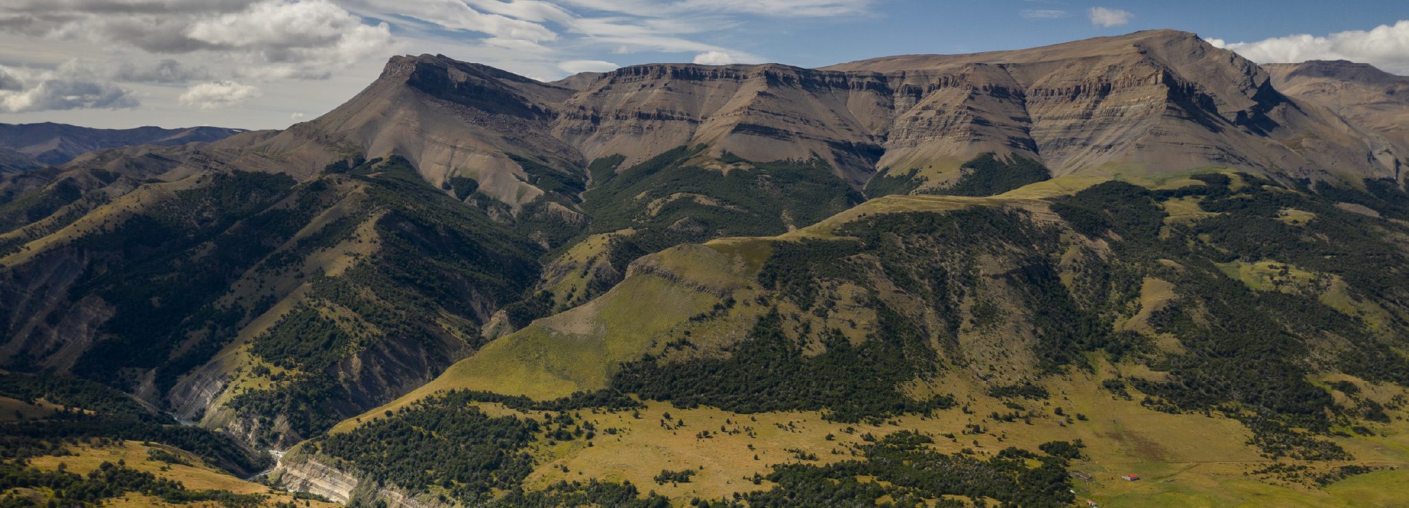 http://Rolling%20green%20hills%20and%20rocky%20cliffs%20forming%20a%20wide%20mountain%20valley.