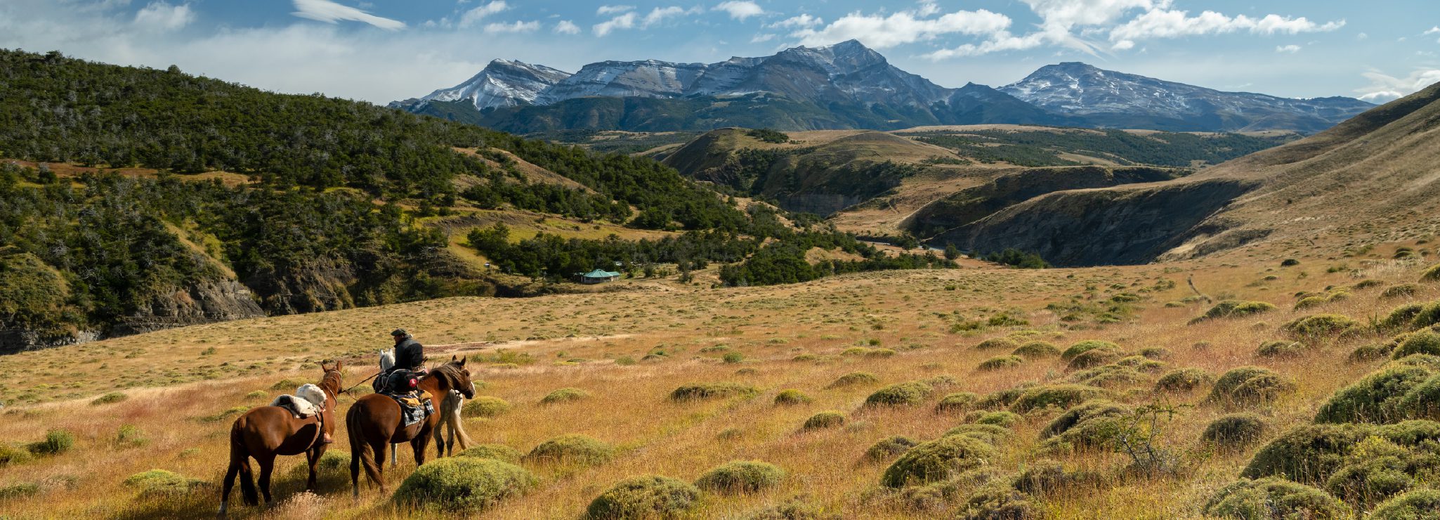 http://Two%20riders%20on%20horseback%20crossing%20an%20open%20grassland%20with%20mountains%20in%20the%20distance.