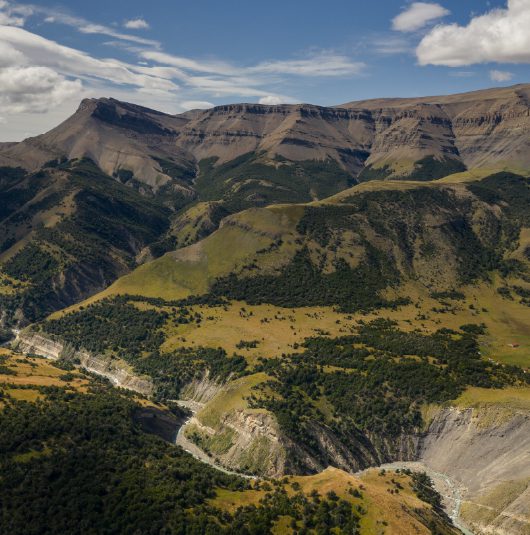http://Rolling%20green%20hills%20and%20rocky%20cliffs%20forming%20a%20wide%20mountain%20valley.