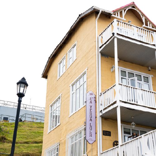 A yellow wooden guesthouse with white balconies on a hillside.