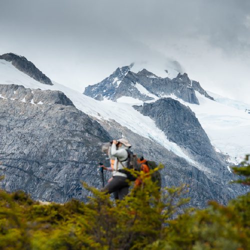 A hiker treks toward rugged, snow-covered mountains.