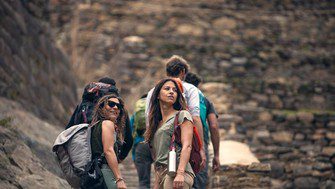 Travelers walk along an ancient Inca stone pathway in Peru, surrounded by historic ruins and terraced walls in the Sacred Valley.