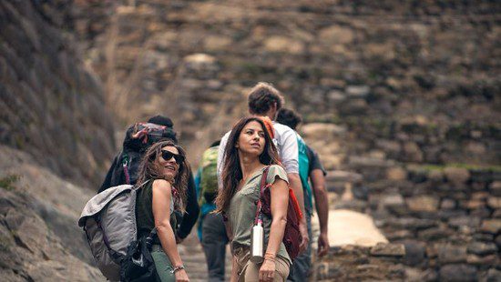Travelers walk along an ancient Inca stone pathway in Peru, surrounded by historic ruins and terraced walls in the Sacred Valley.