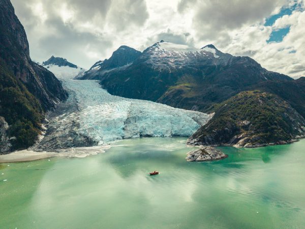 http://A%20large%20glacier%20descends%20between%20dark%20mountains%20into%20a%20milky%20turquoise%20lake,%20where%20a%20small%20boat%20floats%20near%20the%20ice%20under%20a%20cloudy%20sky.