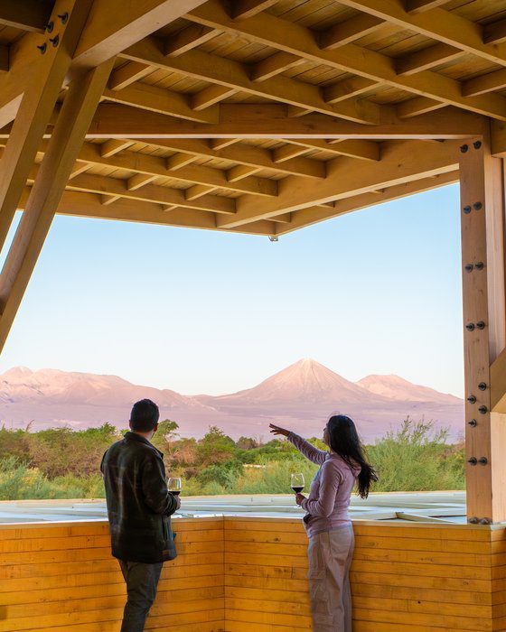 Casal com taças de vinho apreciando a vista do vulcão Licancabur no pôr do sol do deserto do Atacama no Lodge Explora