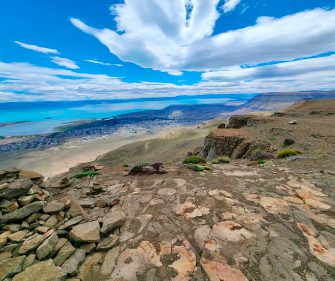 Hiker's viewpoint from a rocky summit overlooking the electric blue Lago Argentino and the town of El Calafate, Patagonia, Argentina