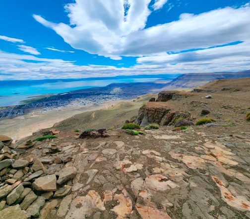 Hiker's viewpoint from a rocky summit overlooking the electric blue Lago Argentino and the town of El Calafate, Patagonia, Argentina