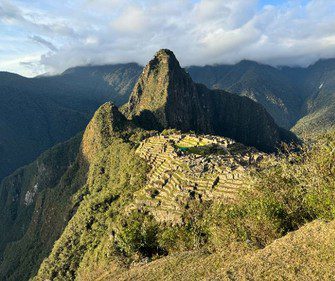 Panoramic view of Machu Picchu in Peru at golden hour, showcasing iconic Inca ruins set against misty Andean peaks.