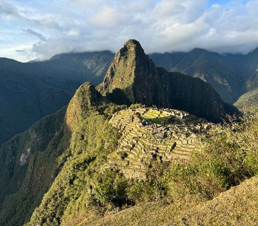 Panoramic view of Machu Picchu in Peru at golden hour, showcasing iconic Inca ruins set against misty Andean peaks.