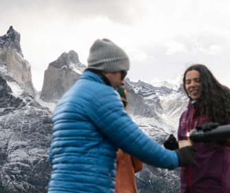 Tour guide welcoming travelers in winter clothing with snow-covered Patagonian mountains in the background, Torres del Paine