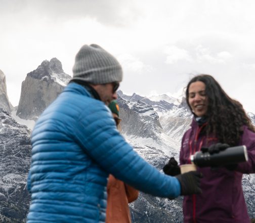 Tour guide welcoming travelers in winter clothing with snow-covered Patagonian mountains in the background, Torres del Paine