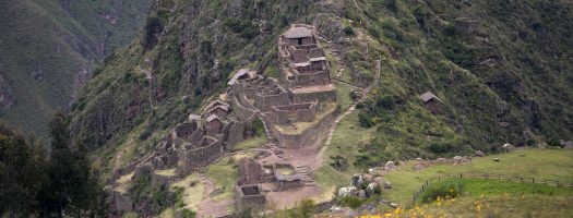 Inca ruins perched on a lush mountainside in Peru’s Sacred Valley, with stone terraces and pathways overlooking the valley below.