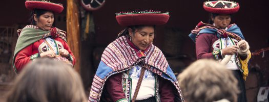 Traditional Andean artisans demonstrate cultural practices for visitors in Peru’s Sacred Valley, wearing vivid handmade textiles.