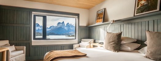 Cozy hotel bedroom with large window framing panoramic views of Torres del Paine mountains