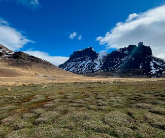 Wide open Patagonian steppe with rugged snow-dusted volcanic peaks and green tundra grasslands under a bright blue sky, Sierra Baguales, Chile