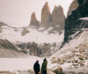 Two hikers standing before the iconic Torres del Paine granite towers covered in snow and ice in Torres del Paine National Park, Chilean Patagonia