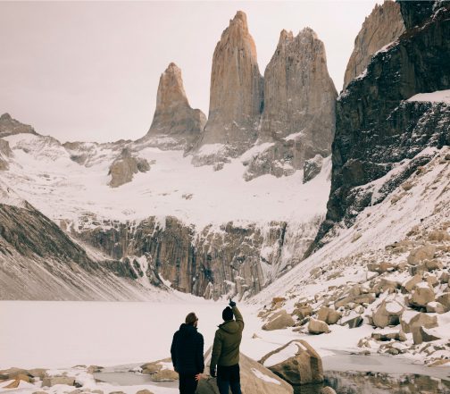 Two hikers standing before the iconic Torres del Paine granite towers covered in snow and ice in Torres del Paine National Park, Chilean Patagonia
