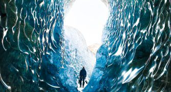 Solo explorer inside a Vatnajökull ice cave, Iceland — sculpted blue glacial walls and natural light tunnel