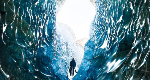 Solo explorer inside a Vatnajökull ice cave, Iceland — sculpted blue glacial walls and natural light tunnel