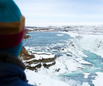 Winter expedition in Iceland — traveler overlooking Gullfoss frozen waterfall and glacial canyon