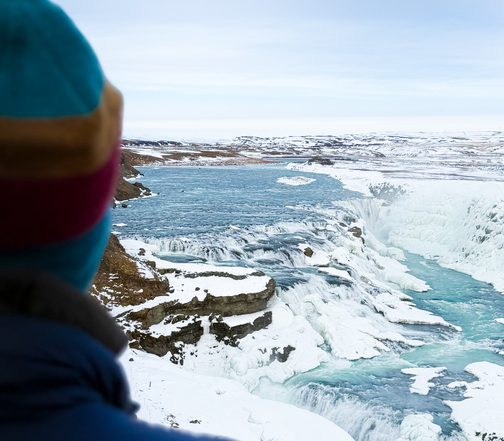 Winter expedition in Iceland — traveler overlooking Gullfoss frozen waterfall and glacial canyon
