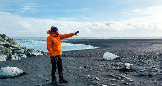 Explora guide pointing across Iceland's black sand beach with glacial ice chunks washed ashore on the South Coast