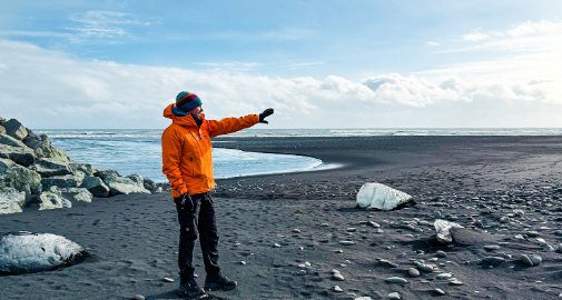 Explora guide pointing across Iceland's black sand beach with glacial ice chunks washed ashore on the South Coast
 
