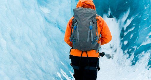 Expedition traveler with backpack exploring deep inside a blue ice crevasse on Vatnajökull glacier, Iceland